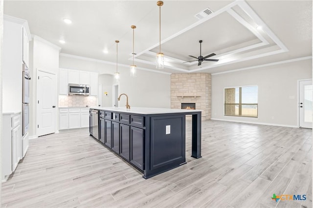 kitchen with decorative light fixtures, appliances with stainless steel finishes, a raised ceiling, an island with sink, and white cabinets