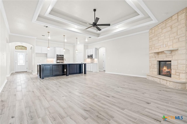 unfurnished living room featuring crown molding, a fireplace, a tray ceiling, and light hardwood / wood-style flooring