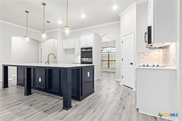 kitchen featuring light hardwood / wood-style flooring, white cabinetry, backsplash, an island with sink, and decorative light fixtures