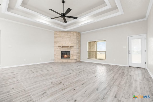 unfurnished living room featuring a stone fireplace, light hardwood / wood-style flooring, ornamental molding, and a raised ceiling