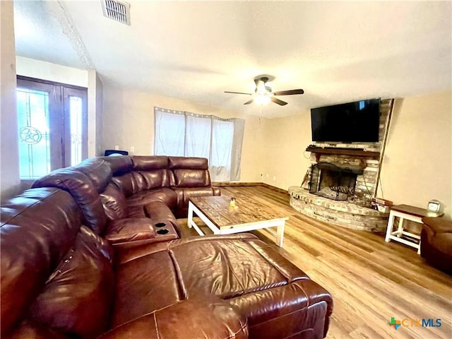 living room with ceiling fan, wood-type flooring, and a stone fireplace