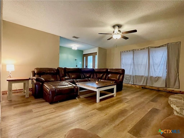 living room with ceiling fan, light wood-type flooring, and a textured ceiling