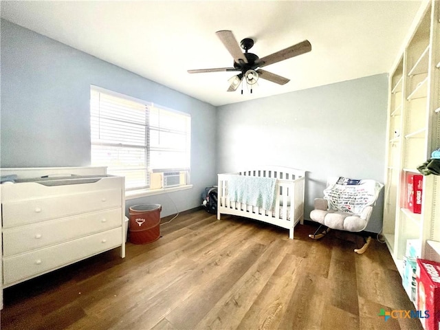 bedroom featuring cooling unit, wood-type flooring, a nursery area, and ceiling fan