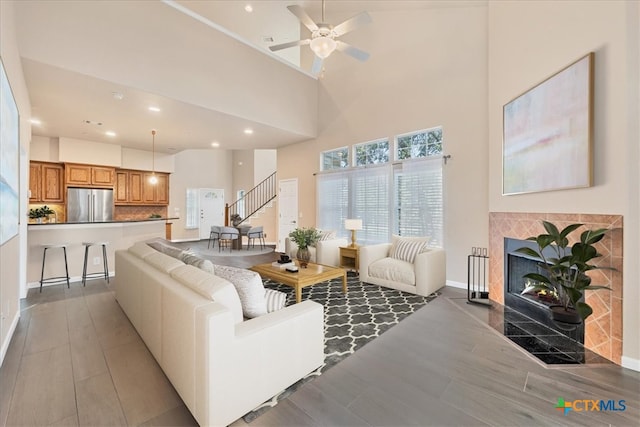 living room with a high ceiling, a tile fireplace, hardwood / wood-style floors, and ceiling fan