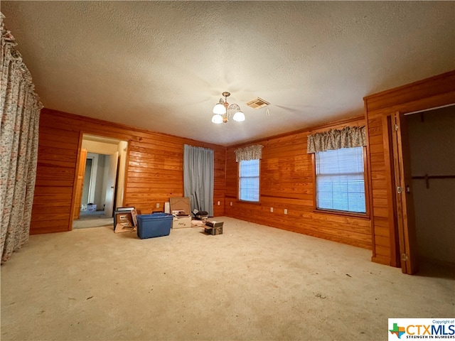 unfurnished room featuring an inviting chandelier, light colored carpet, wooden walls, and a textured ceiling