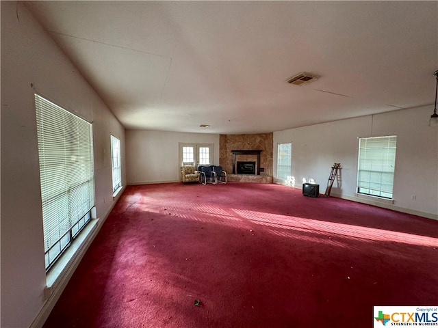 unfurnished living room featuring a stone fireplace and carpet floors