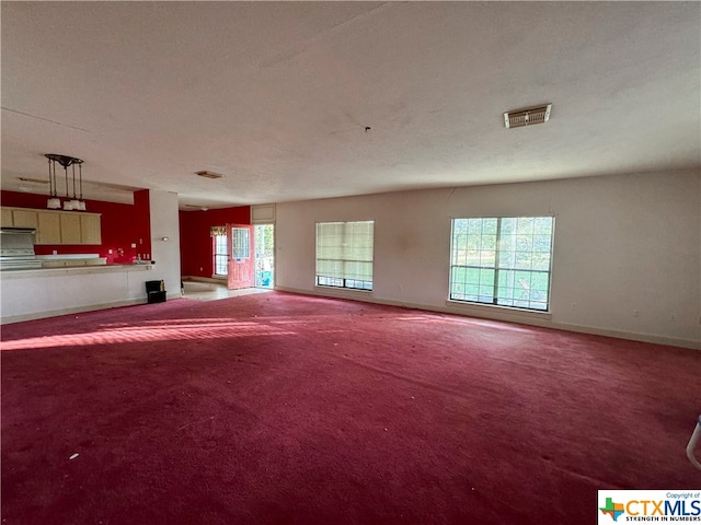 unfurnished living room with a wealth of natural light, a textured ceiling, and carpet