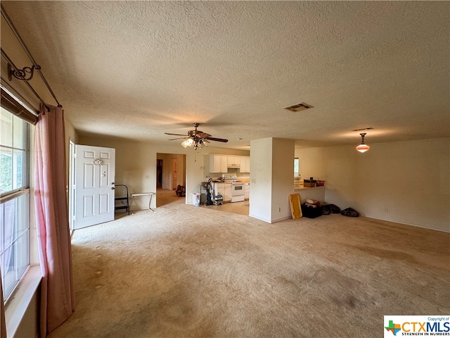 unfurnished living room with a textured ceiling, light colored carpet, and ceiling fan