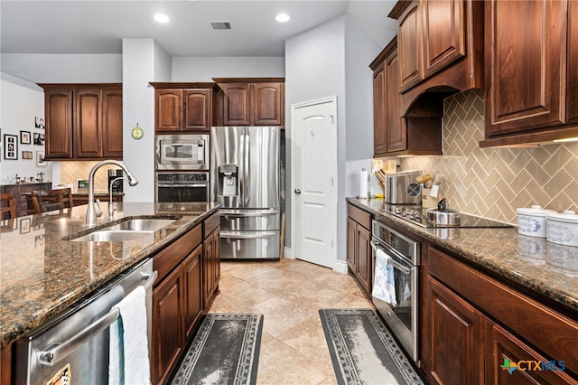 kitchen featuring sink, appliances with stainless steel finishes, dark stone counters, light tile patterned floors, and backsplash