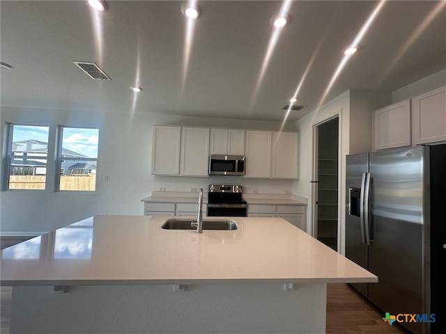 kitchen with appliances with stainless steel finishes, sink, white cabinets, dark hardwood / wood-style floors, and an island with sink