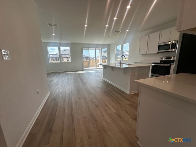 kitchen featuring white cabinetry, sink, stainless steel appliances, an island with sink, and light hardwood / wood-style floors