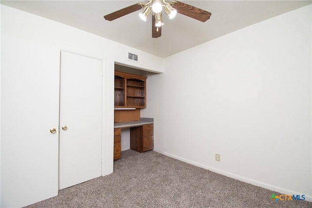 unfurnished bedroom featuring ceiling fan, built in desk, and light colored carpet