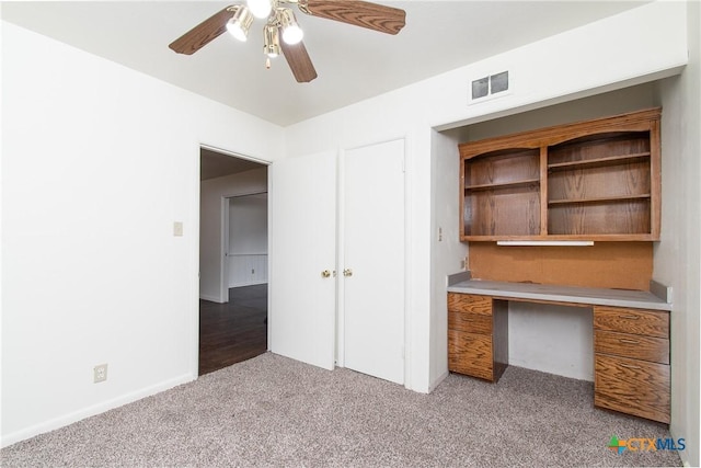 unfurnished office featuring ceiling fan, light colored carpet, and built in desk