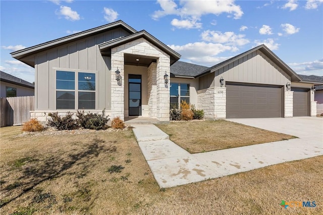 view of front of house with an attached garage, fence, stone siding, driveway, and board and batten siding