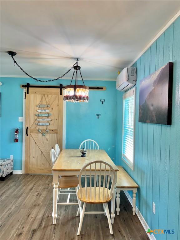 1208 W Adams St, Port Oconnor, TX 77982 - dining space with a wall mounted AC, a barn door, wood finished floors, ornamental molding, and wooden walls