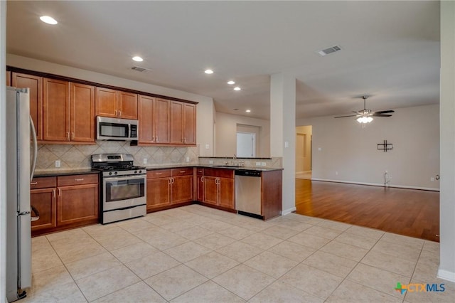7400 Longford Trl, Austin, TX 78754 - kitchen featuring stainless steel appliances, open floor plan, tasteful backsplash, brown cabinets, and light tile patterned flooring