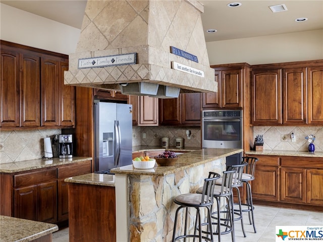 kitchen featuring light stone counters, decorative backsplash, stainless steel fridge with ice dispenser, and a kitchen island