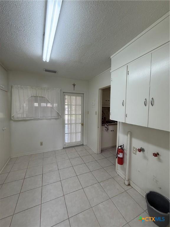 clothes washing area with a textured ceiling and light tile patterned floors