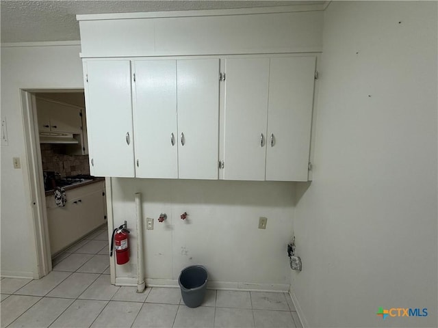 clothes washing area featuring a textured ceiling, cabinets, and light tile patterned floors