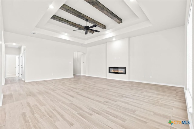 unfurnished living room featuring a tray ceiling, ceiling fan, light hardwood / wood-style flooring, and beam ceiling