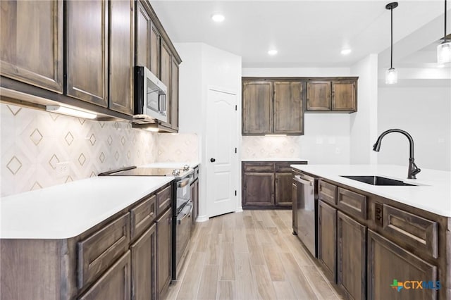 kitchen with appliances with stainless steel finishes, sink, light hardwood / wood-style floors, hanging light fixtures, and an island with sink