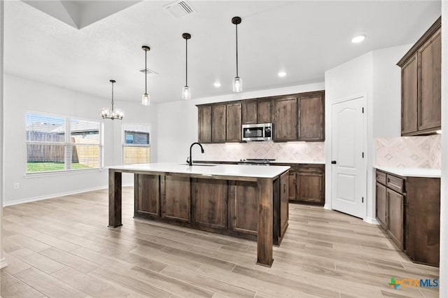 kitchen with backsplash, an inviting chandelier, a center island with sink, decorative light fixtures, and dark brown cabinets