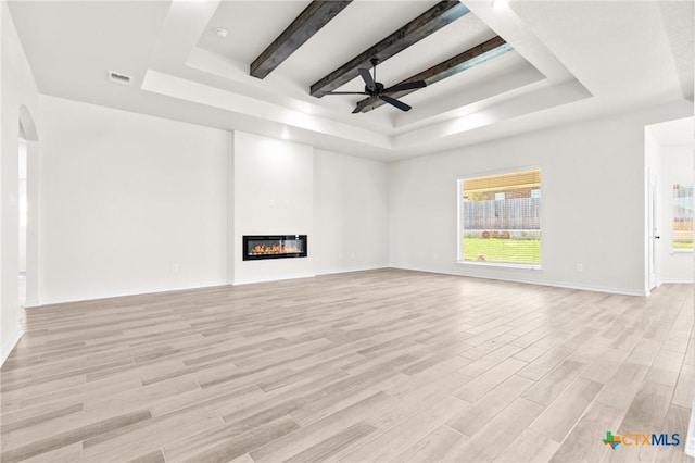 unfurnished living room featuring a tray ceiling, ceiling fan, and light wood-type flooring