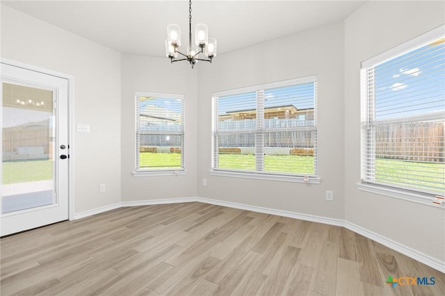 unfurnished dining area featuring plenty of natural light, light wood-type flooring, and a notable chandelier