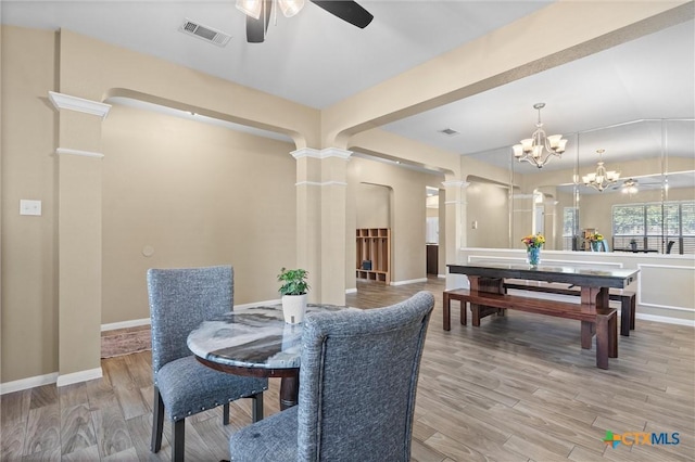 dining space with light wood-type flooring, visible vents, decorative columns, and ceiling fan with notable chandelier