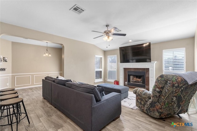 living area featuring ceiling fan with notable chandelier, a fireplace, visible vents, light wood-style floors, and vaulted ceiling