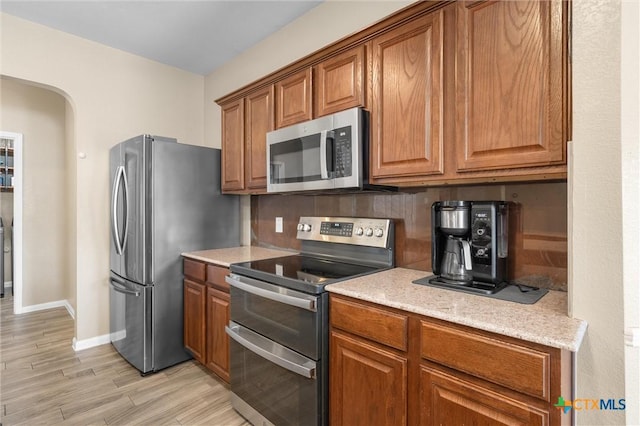 kitchen with arched walkways, stainless steel appliances, backsplash, and brown cabinets