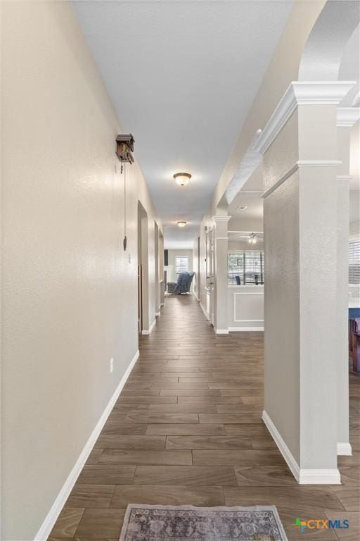 hall featuring decorative columns, baseboards, and wood finished floors