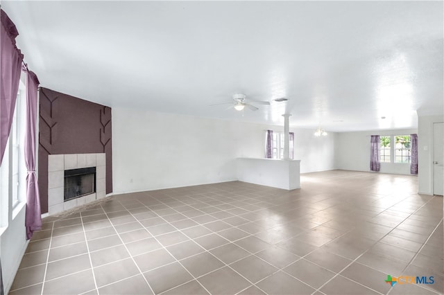 unfurnished living room with a tile fireplace, light tile patterned floors, and ceiling fan with notable chandelier