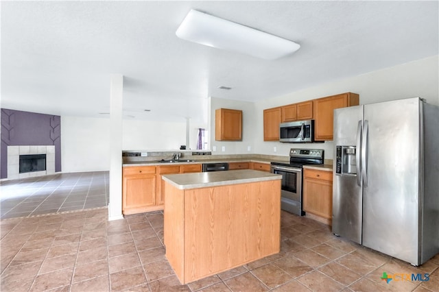 kitchen with a tiled fireplace, stainless steel appliances, sink, light tile patterned floors, and a kitchen island