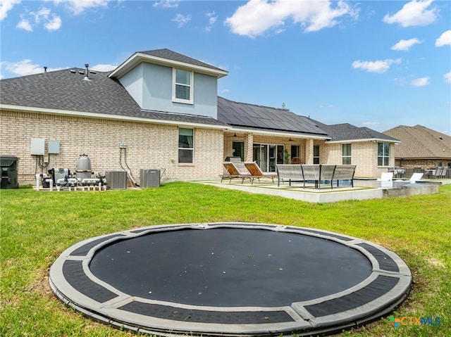 rear view of house featuring brick siding, a trampoline, a lawn, and a patio