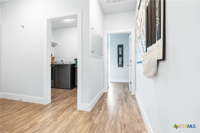 hallway with light wood-type flooring, washer and clothes dryer, and baseboards