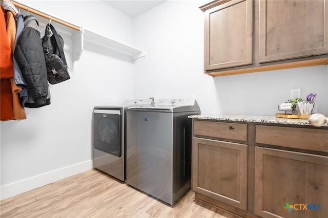 laundry room with cabinet space, washing machine and dryer, baseboards, and light wood-style floors