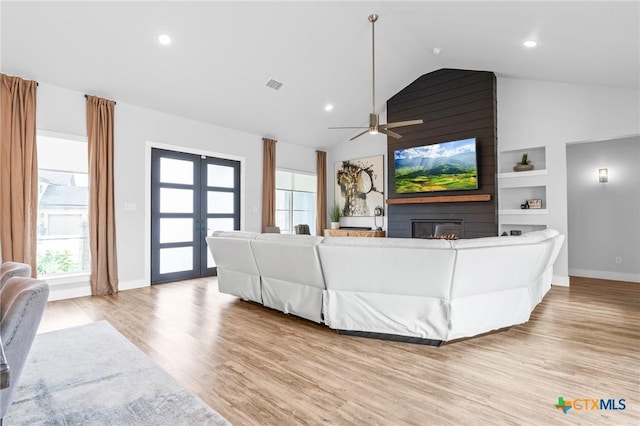 living area featuring a large fireplace, plenty of natural light, visible vents, and wood finished floors