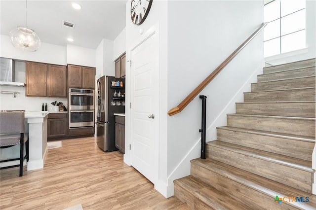 kitchen featuring light wood finished floors, visible vents, wall chimney exhaust hood, stainless steel appliances, and light countertops