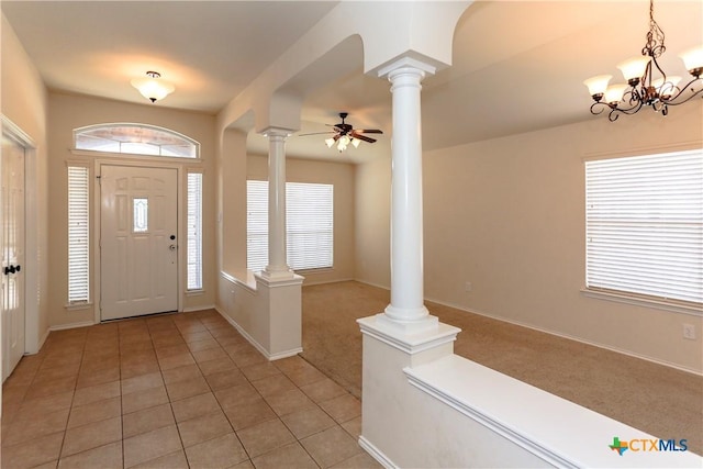 entryway featuring decorative columns, light tile patterned floors, light colored carpet, baseboards, and ceiling fan with notable chandelier