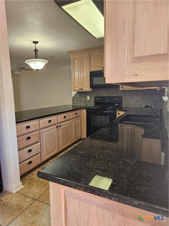 kitchen featuring a peninsula, a sink, light brown cabinetry, black appliances, and backsplash
