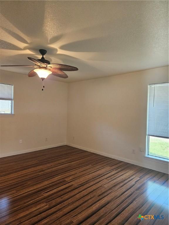spare room featuring a textured ceiling, baseboards, a healthy amount of sunlight, and dark wood finished floors