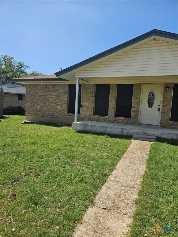 view of front of property with covered porch, a front lawn, and stone siding