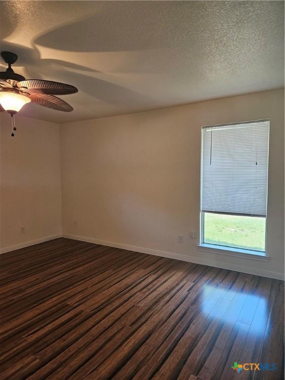spare room featuring a textured ceiling, baseboards, ceiling fan, and dark wood-style floors