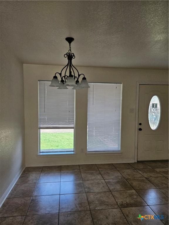 unfurnished dining area featuring baseboards, a chandelier, and a textured ceiling