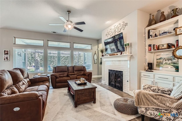 living room with light wood-type flooring, visible vents, a ceiling fan, baseboards, and a brick fireplace