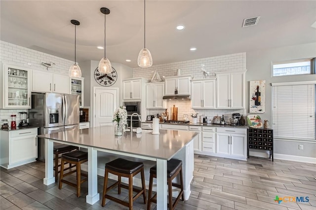 kitchen with visible vents, backsplash, under cabinet range hood, a breakfast bar, and stainless steel appliances