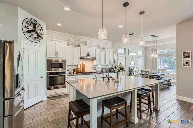 kitchen featuring a breakfast bar, under cabinet range hood, white cabinetry, appliances with stainless steel finishes, and decorative backsplash