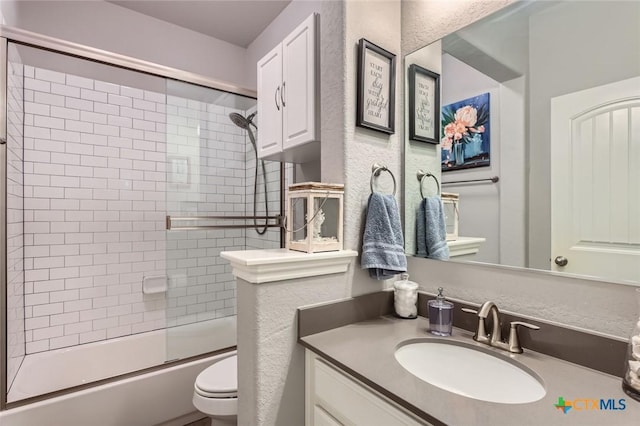 full bathroom with combined bath / shower with glass door, toilet, vanity, and a textured wall