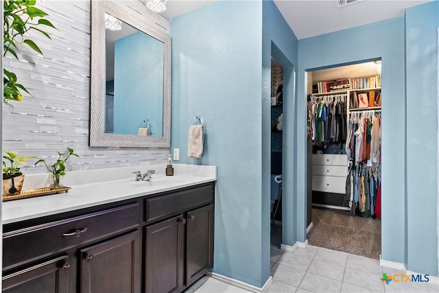 bathroom featuring a walk in closet, vanity, baseboards, and tile patterned flooring